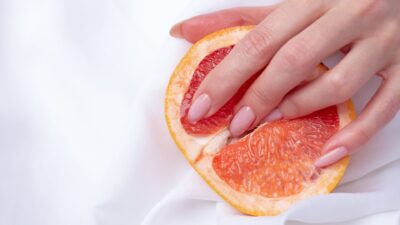 Női kéz grapefruitra helyezve fehér háttéren – ujjvibrátor és érzéki érintés